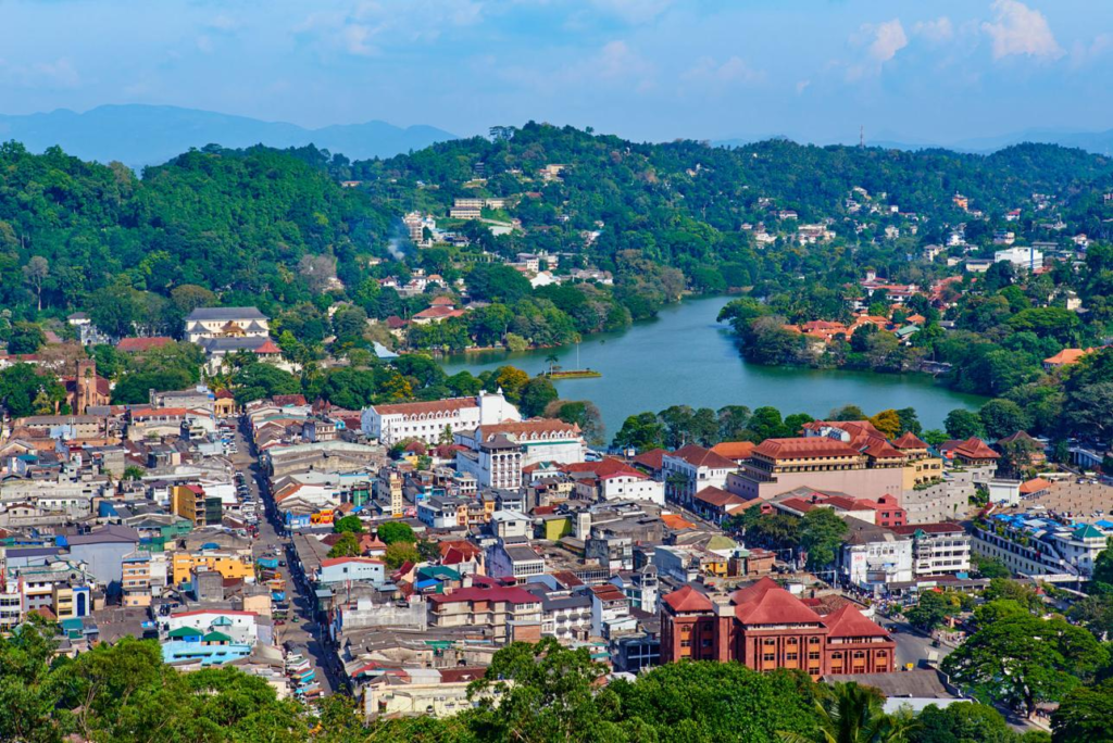 A panoramic aerial view of Kandy showing the cityscape, surrounding mountains, and Kandy Lake in Sri Lanka.