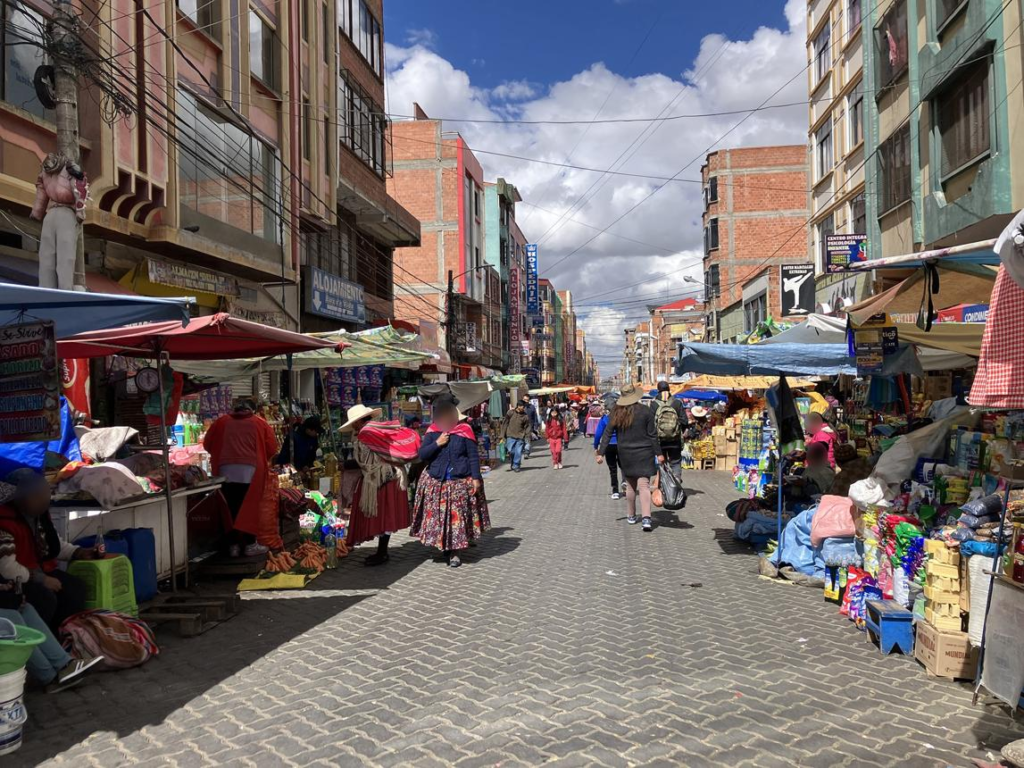 Visitors walking through busy streets in El Alto with markets, shops, and pedestrian activity.